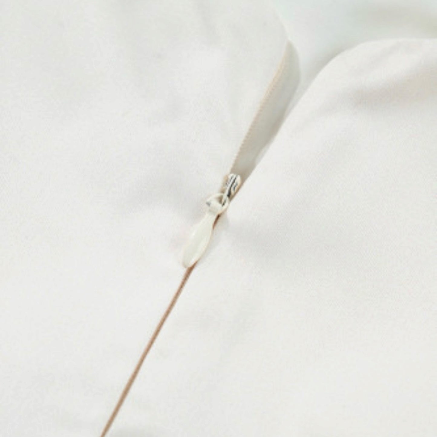 Beige fabric with a small zipper pull, close-up detail of a babydoll dress